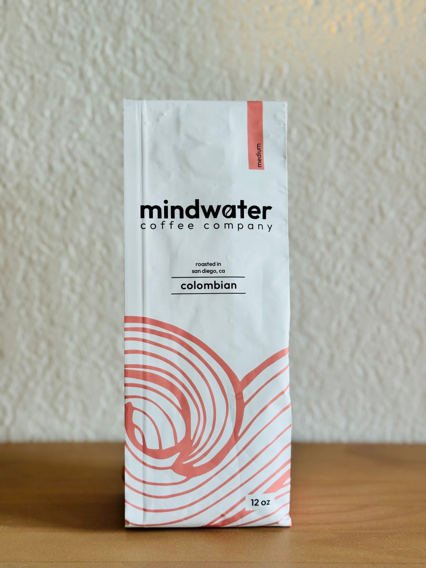 12 oz medium roast colombian coffee package from mindwater coffee company on a wooden surface with a neutral background