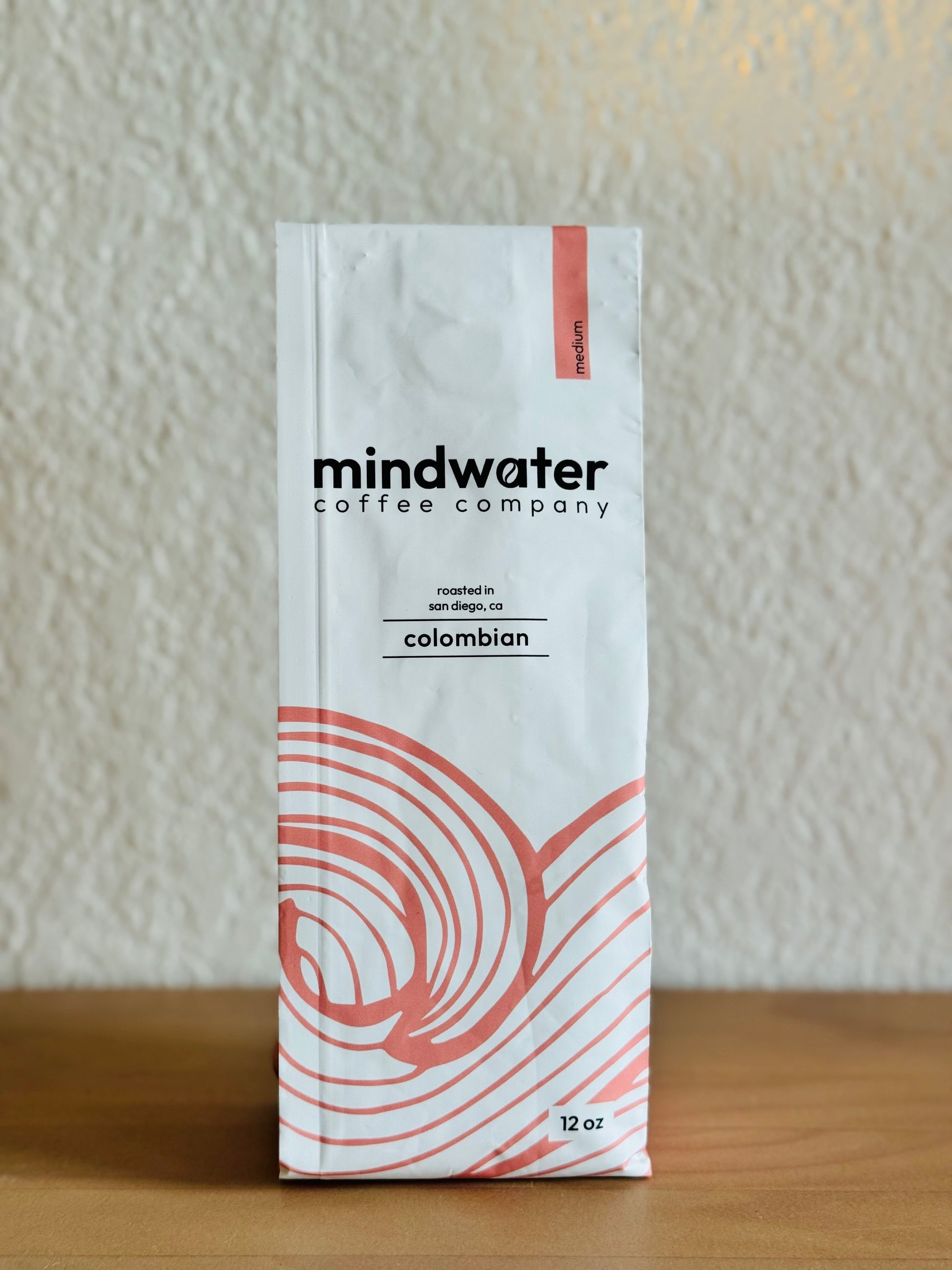12 oz medium roast colombian coffee package from mindwater coffee company on a wooden surface with a neutral background